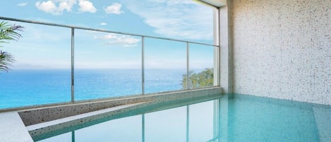 A clear view of a swimming pool with a glass barrier, a view of the ocean, and a speckled wall.
