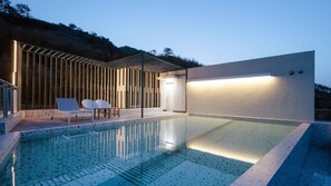 A modern outdoor pool area with a clear glass surface, a wooden pergola, and two white lounge chairs. - The Beige (Geoje)