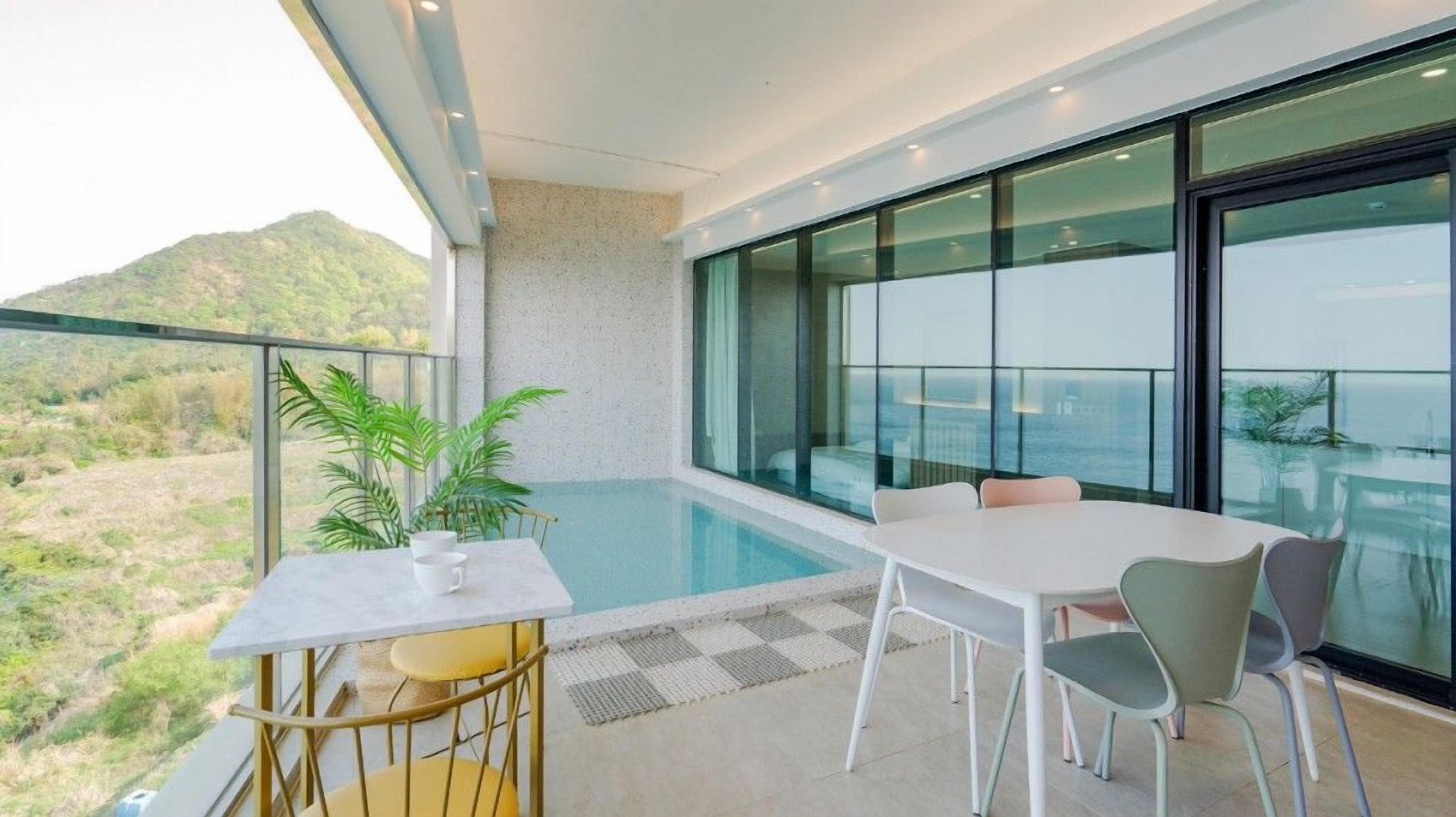 A modern balcony with a pool, a table, and chairs, overlooking a mountainous landscape.