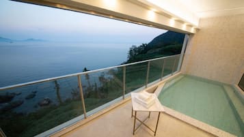 A balcony with a glass railing overlooking a body of water and greenery.