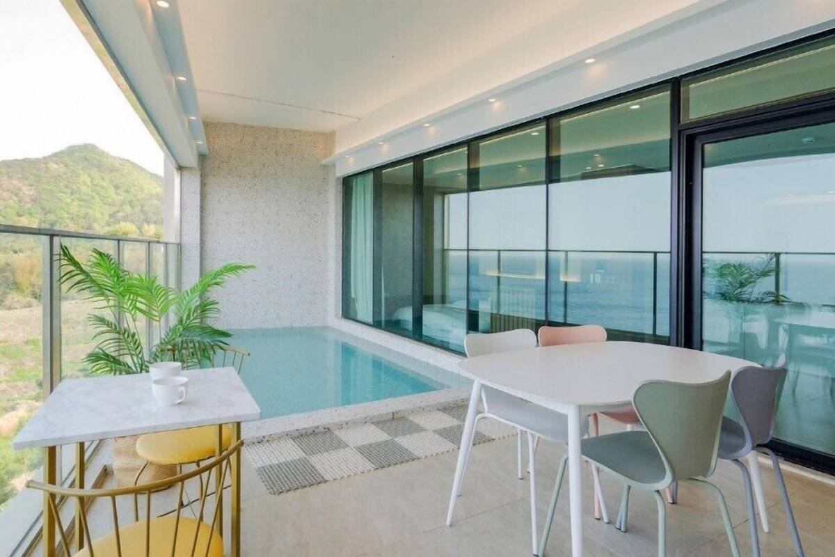 A modern balcony with a pool, a table, and chairs, overlooking a mountainous landscape.