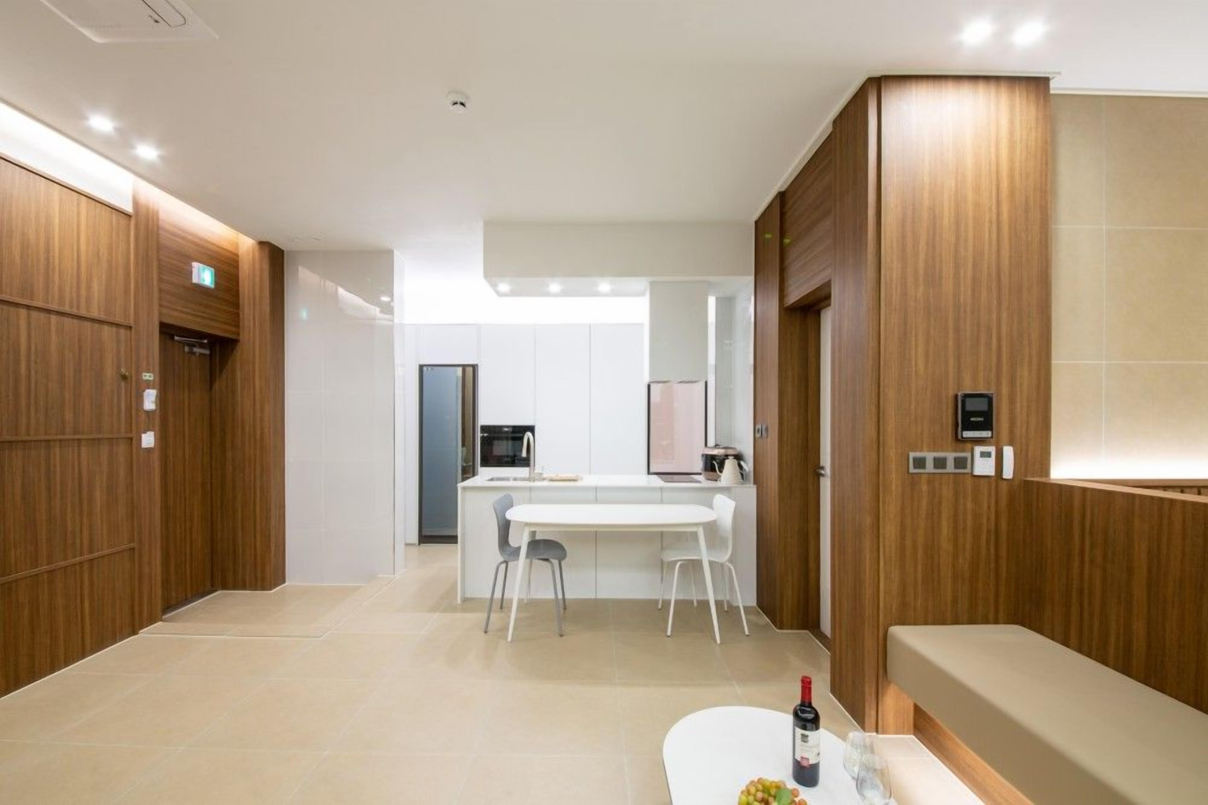 A modern hotel room with a wooden panel wall, a white dining area, and a small kitchenette.