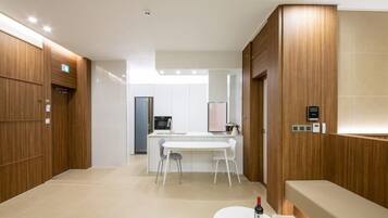 A modern hotel room with a wooden panel wall, a white dining area, and a small kitchenette.