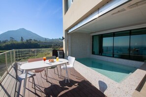 A modern outdoor pool area with a table and chairs, a glass balustrade, and a mountain view. - The Beige (Geoje)