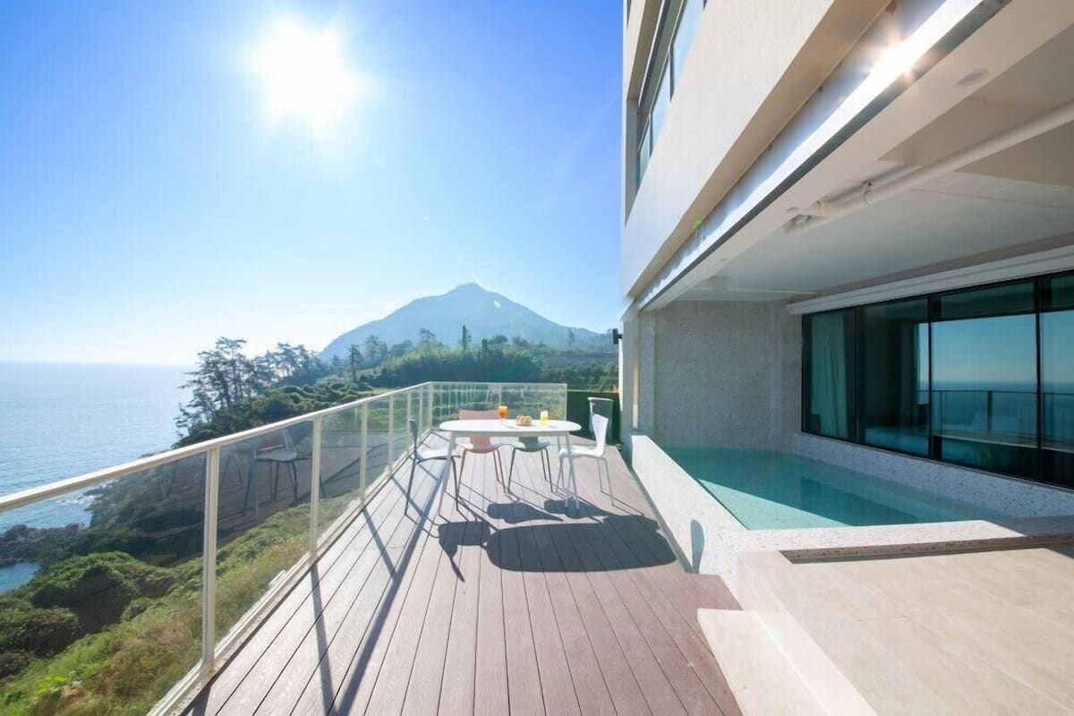 A modern balcony with a wooden deck, a glass railing, and a table with chairs.