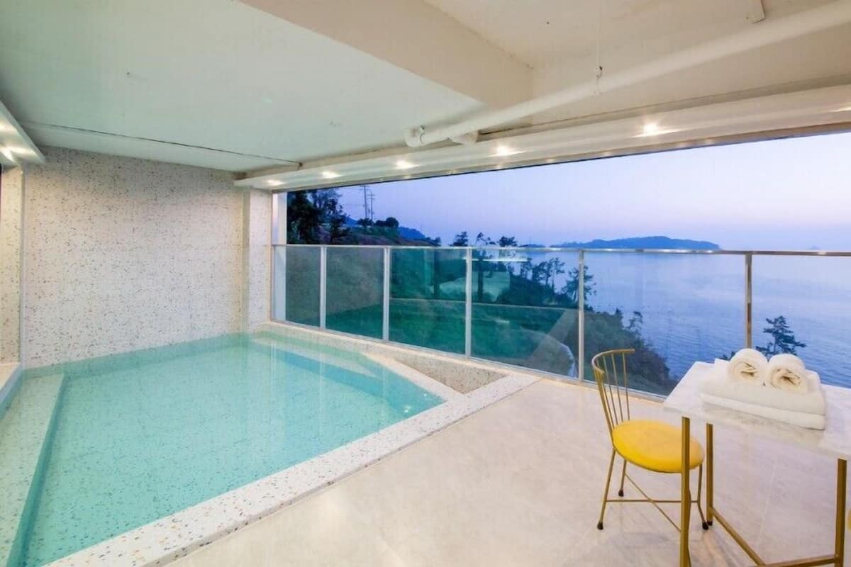 A modern indoor swimming pool with a glass balustrade overlooking a scenic ocean view.