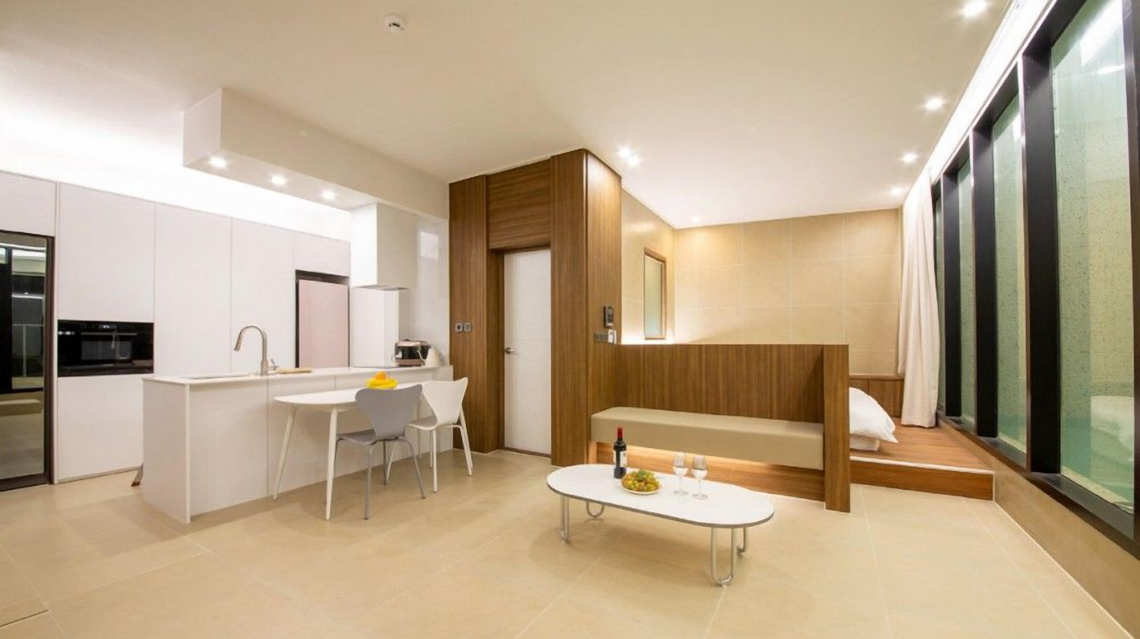 A modern kitchen with white cabinets, a dining area with a white table and chairs, and a built-in bench with a glass-top table.