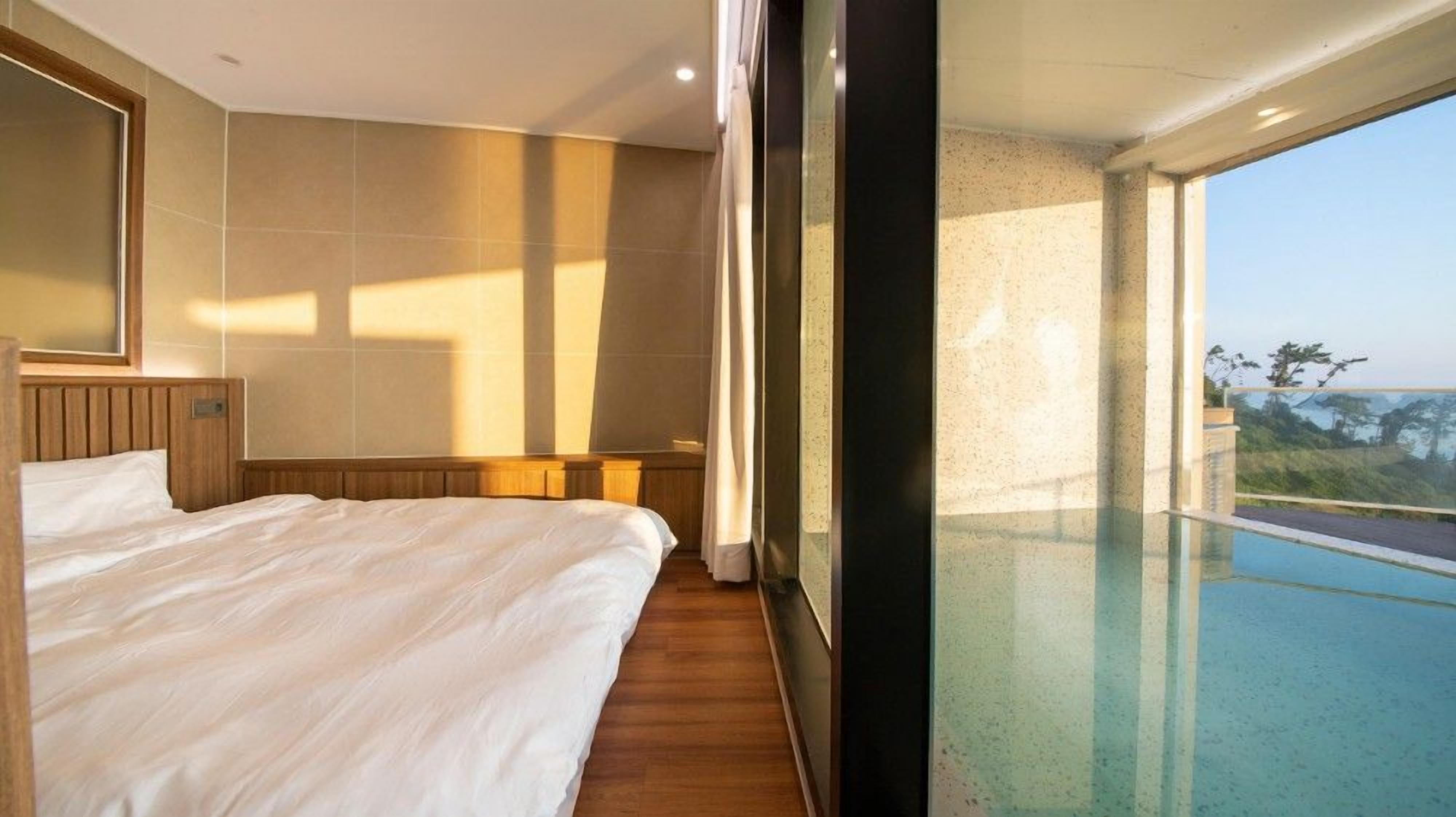 A hotel room with a large bed, a wooden headboard, a large window with a view of a swimming pool and landscape.