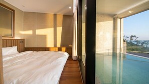 A hotel room with a large bed, a wooden headboard, a large window with a view of a swimming pool and landscape. - The Beige (Geoje)