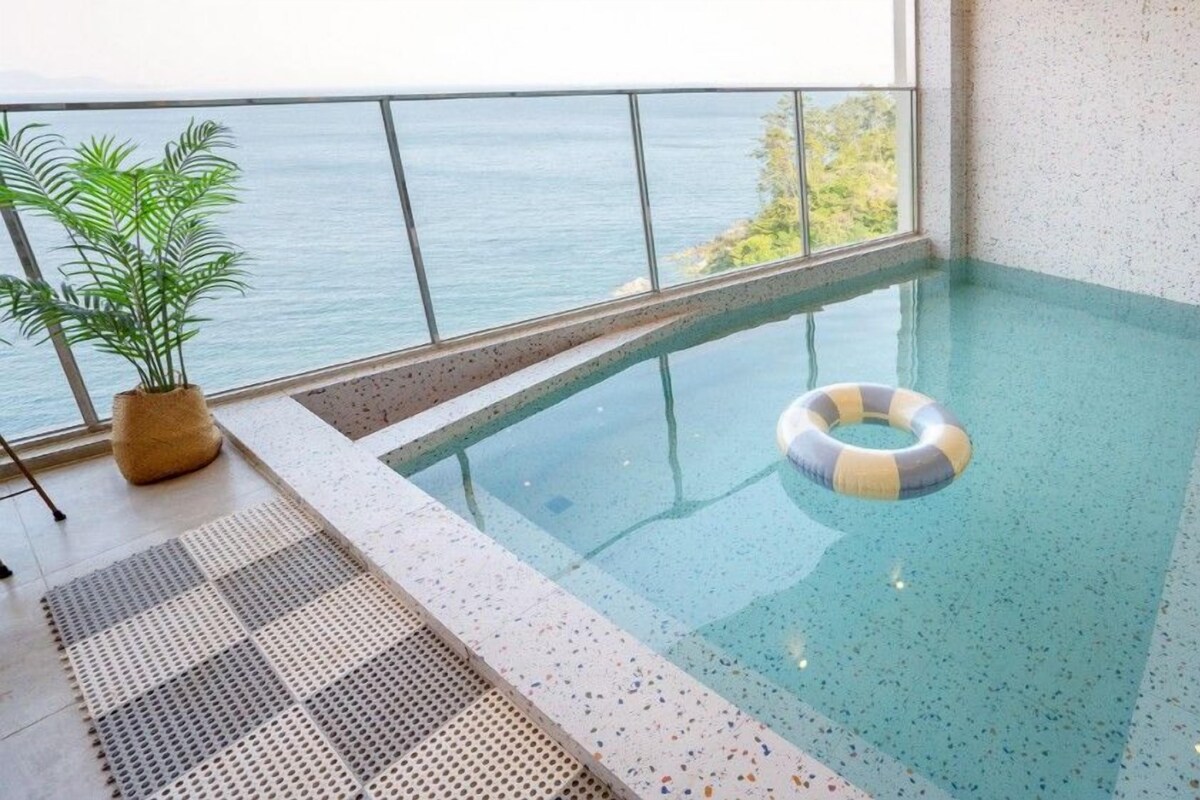 A small indoor swimming pool with a clear view of the sea through large windows.