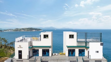 Un hotel costero con dos edificios blancos, un espacio de estar al aire libre cubierto y vista al mar y la costa distante.