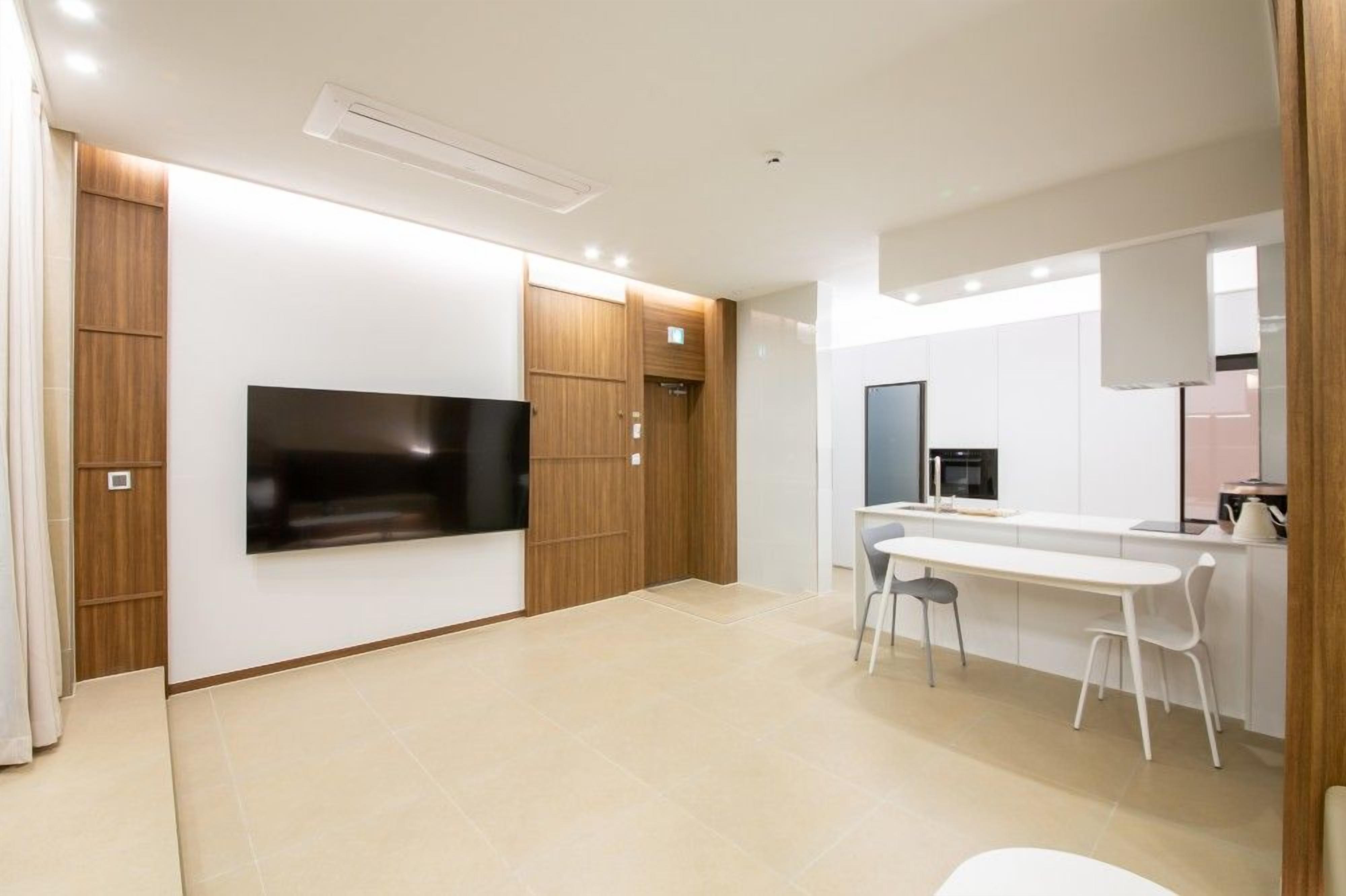 A modern kitchen with a built-in oven, a dining area with a white table and chairs, and a flat-screen TV mounted on the wall.