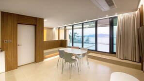 A modern room with a large window, a round table with chairs, and a wooden accent wall. - The Beige (Geoje)