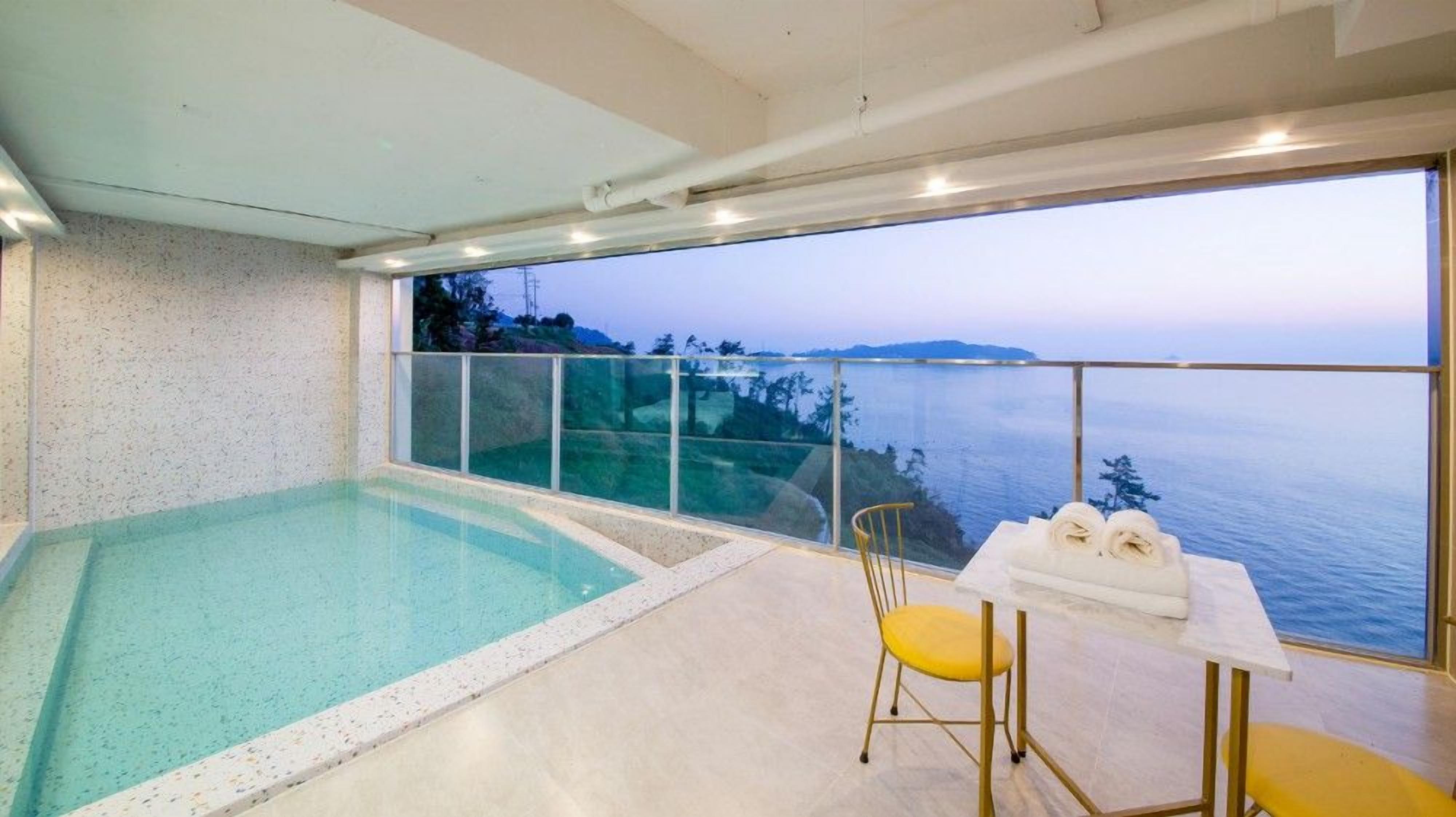 A modern indoor swimming pool with a glass balustrade overlooking a scenic ocean view.