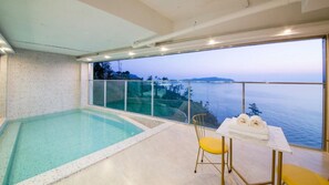 A modern indoor swimming pool with a glass balustrade overlooking a scenic ocean view. - The Beige (Geoje)