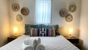 A neatly made bed with rolled towels, a patterned headboard, and decorative wall hangings. - Modern Rustic Retreat in Poconos (Greentown)