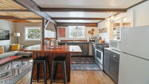 A kitchen with a central island, wooden beams, a sink, stove, and a refrigerator. - Modern Rustic Retreat in Poconos (Greentown)