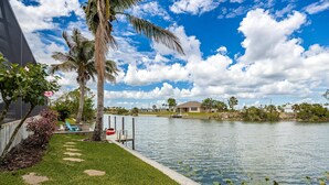 A serene outdoor area with a water body, palm trees, and a lawn. - Where waters intersect and Dreams unwind! Kayak, Bikes, Heated Pool & Spa - Villa Cayman - Roelens (Cape Coral)