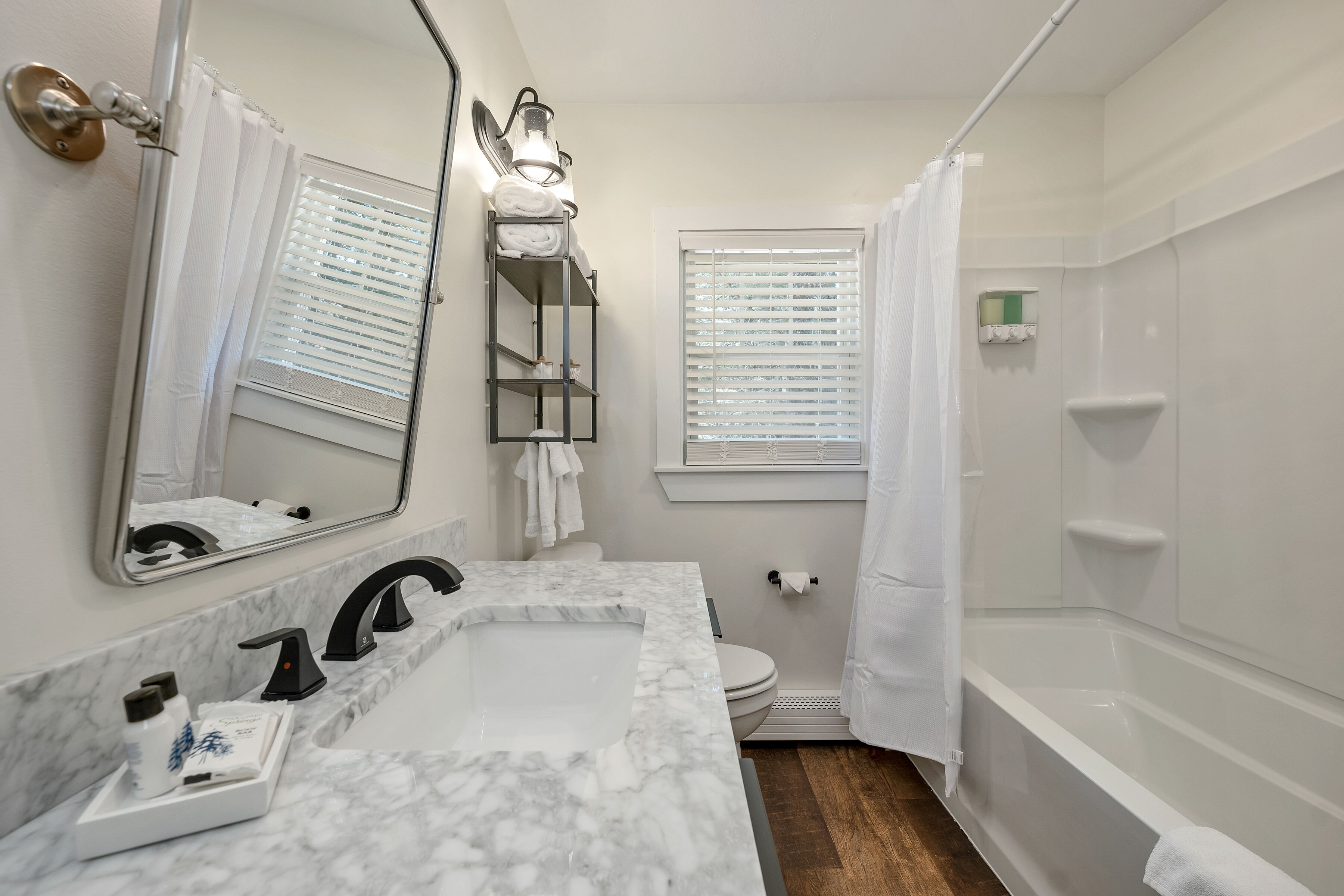 A bathroom with a marble sink, a toilet, a shower, and a window with blinds.