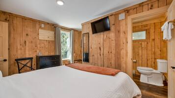 Una stanza con rivestimento in legno, un letto, una cassettiera, un televisore e un water.