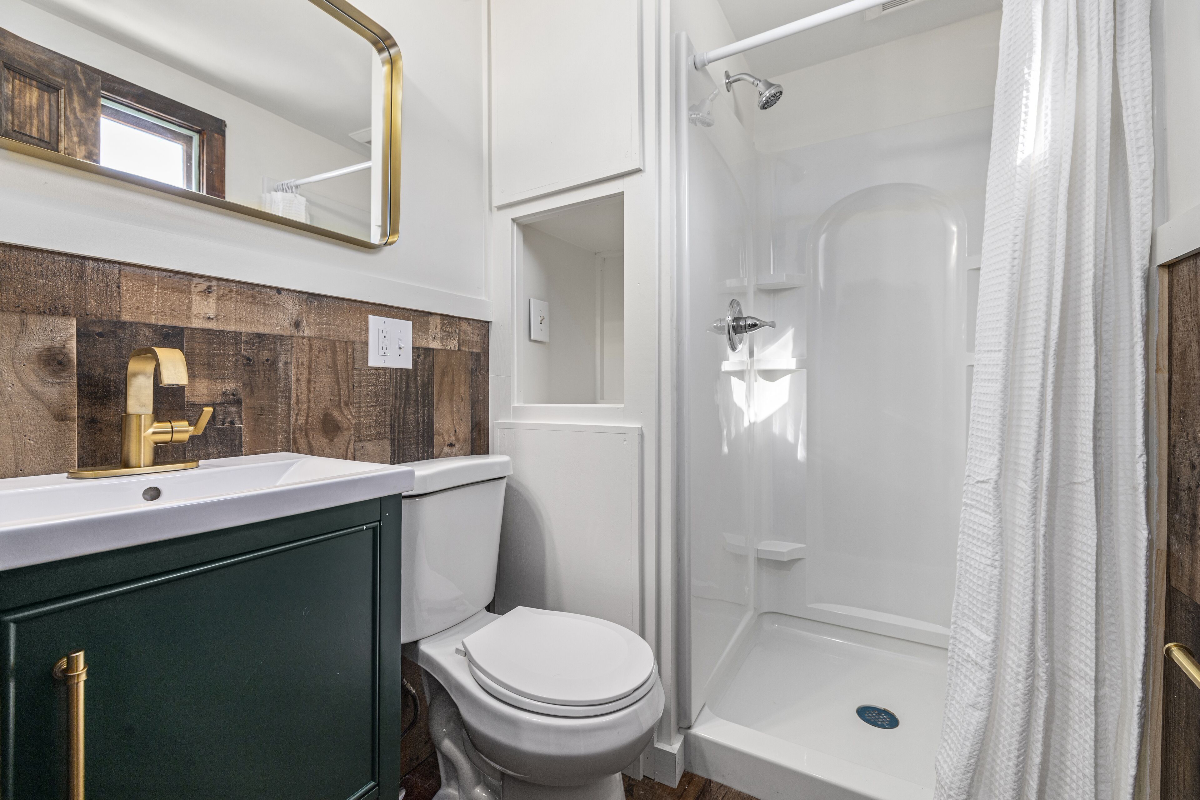 Ein Badezimmer mit Toilette, einer Duschkabine mit Glastür und einem Waschtisch mit Holzverkleidung.