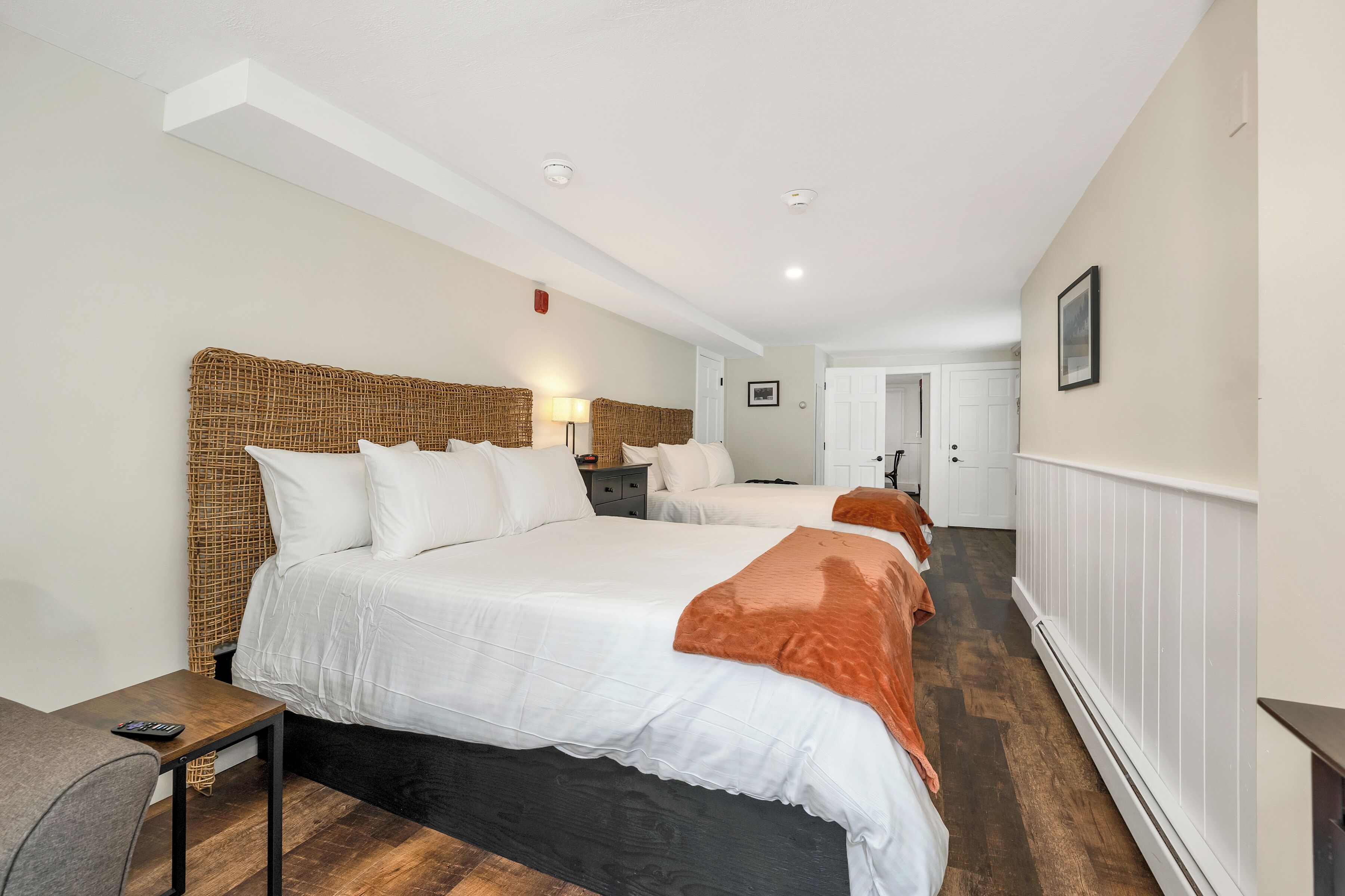 A hotel room with two beds, a bedside table, a lamp, and a chair.