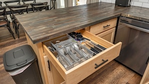 Una cocina con mostrador de madera, lavavajillas y organizador de cajones con utensilios.