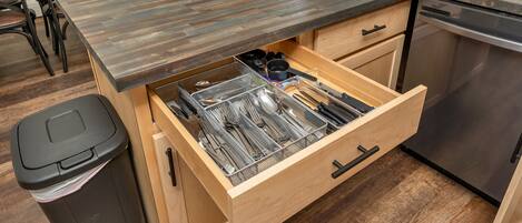 A kitchen with a wooden countertop, a dishwasher, and a drawer organizer with utensils.