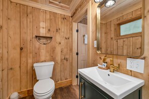 A wooden-paneled bathroom with a white toilet, a sink with a gold faucet, and a mirror above the sink.