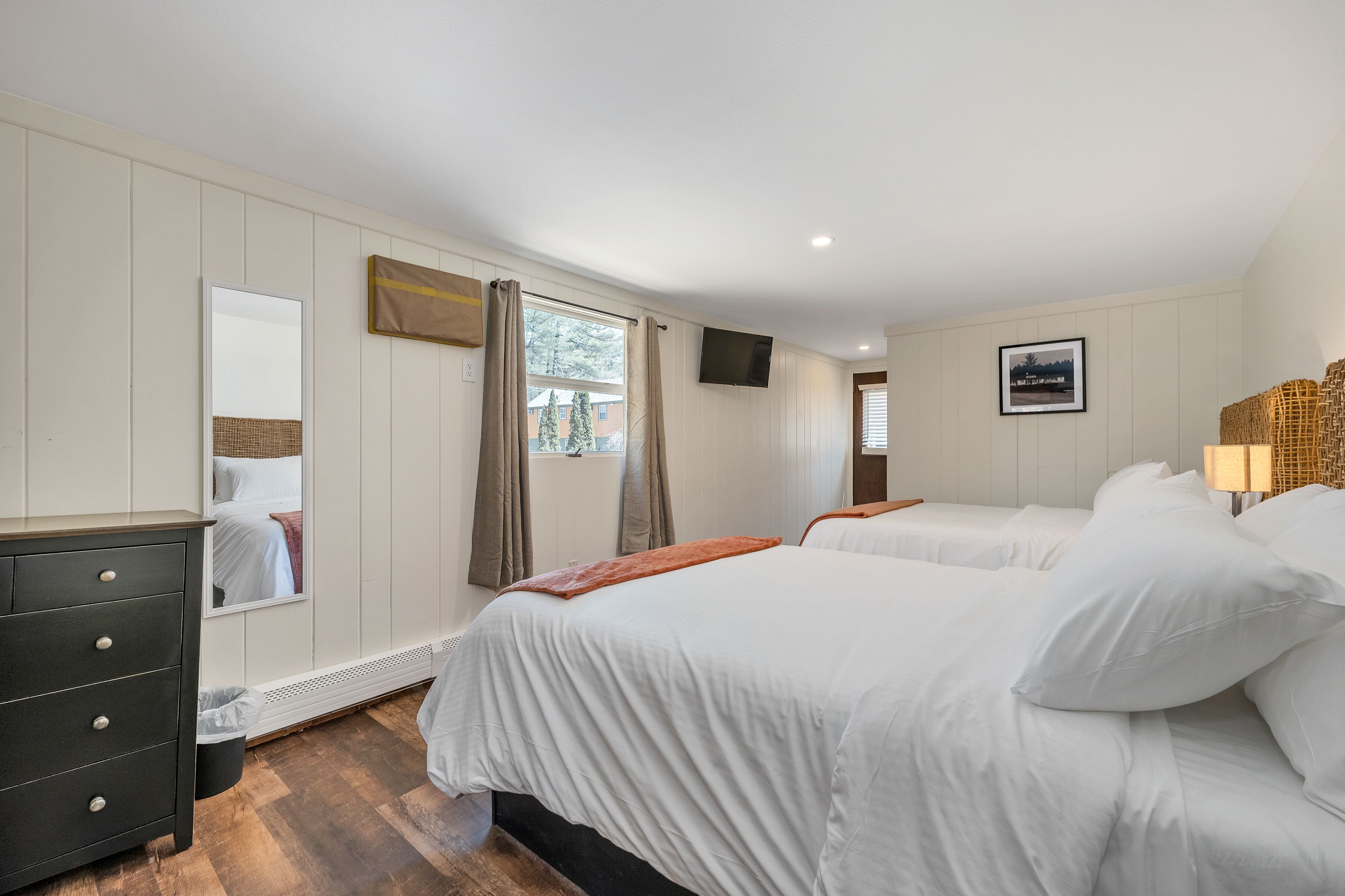 A bedroom with two beds, a dresser, a TV, and a window with curtains.