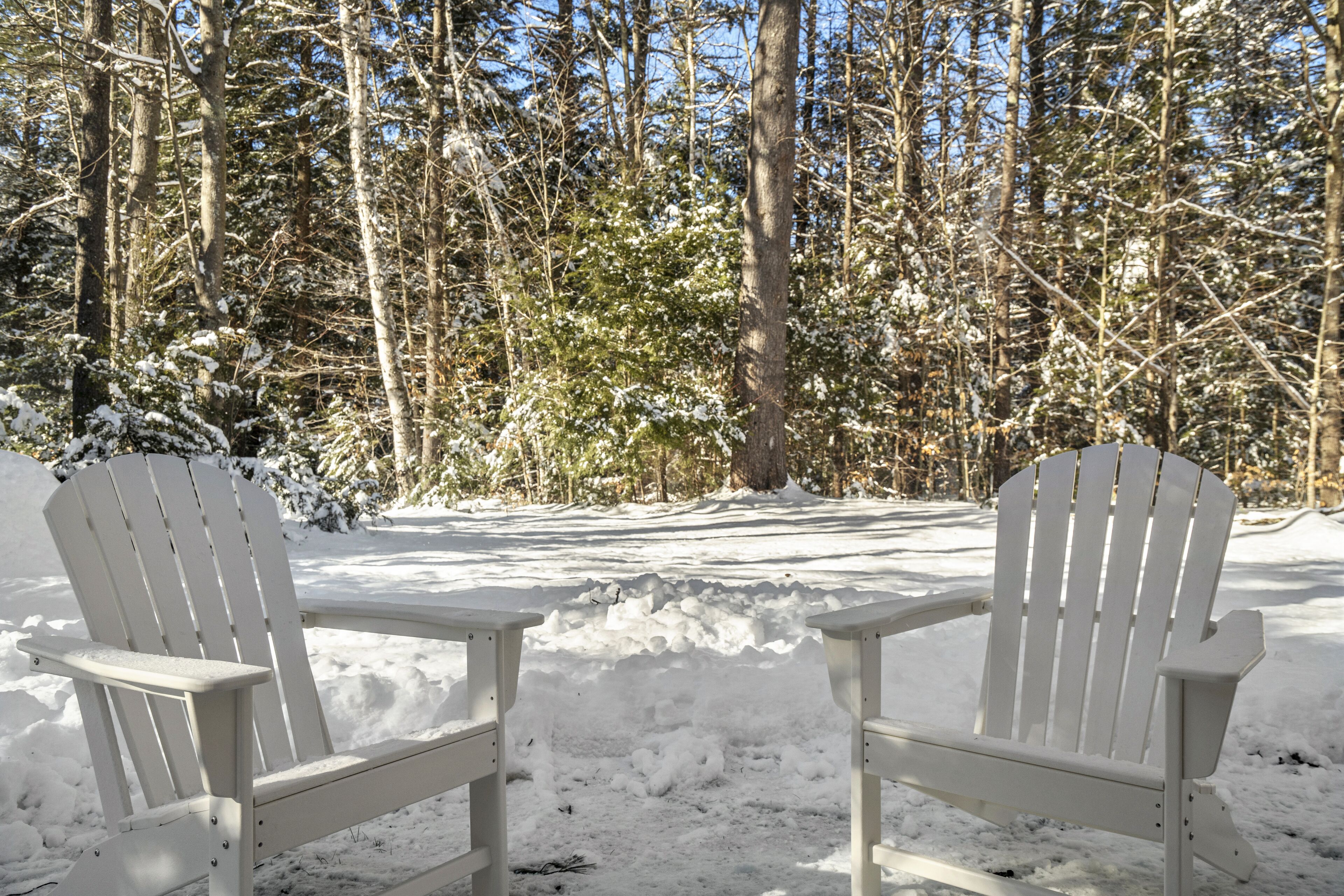 Deux chaises Adirondack blanches, placées dans un décor forestier enneigé.