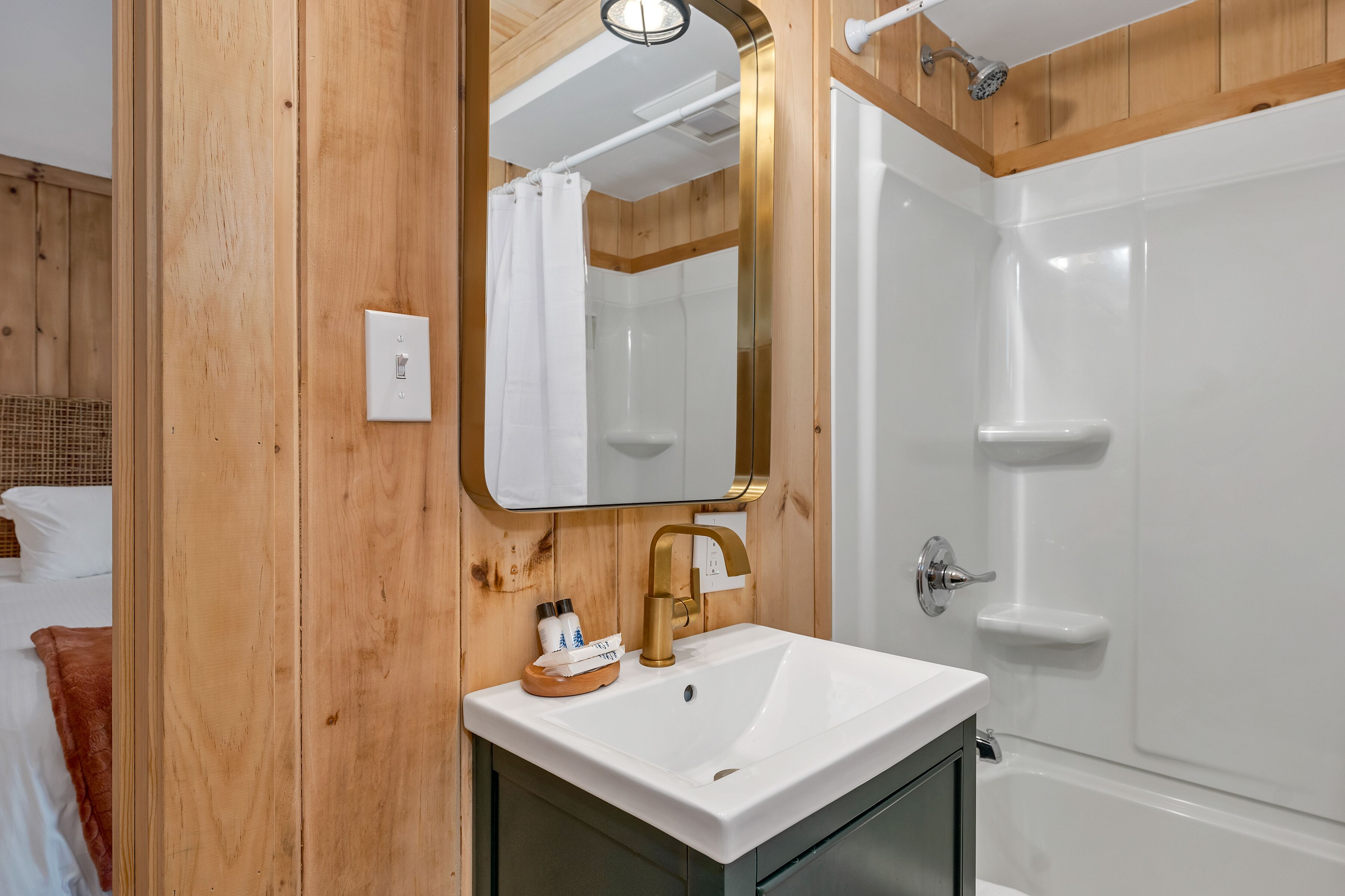 Ein Badezimmer mit einer Holzwand, einem weißen Waschbecken mit goldener Armatur und einer weißen Badewanne.