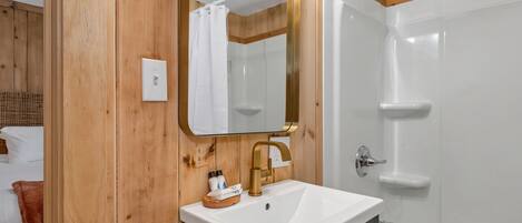 Ein Badezimmer mit einer Holzwand, einem weißen Waschbecken mit goldener Armatur und einer weißen Badewanne.