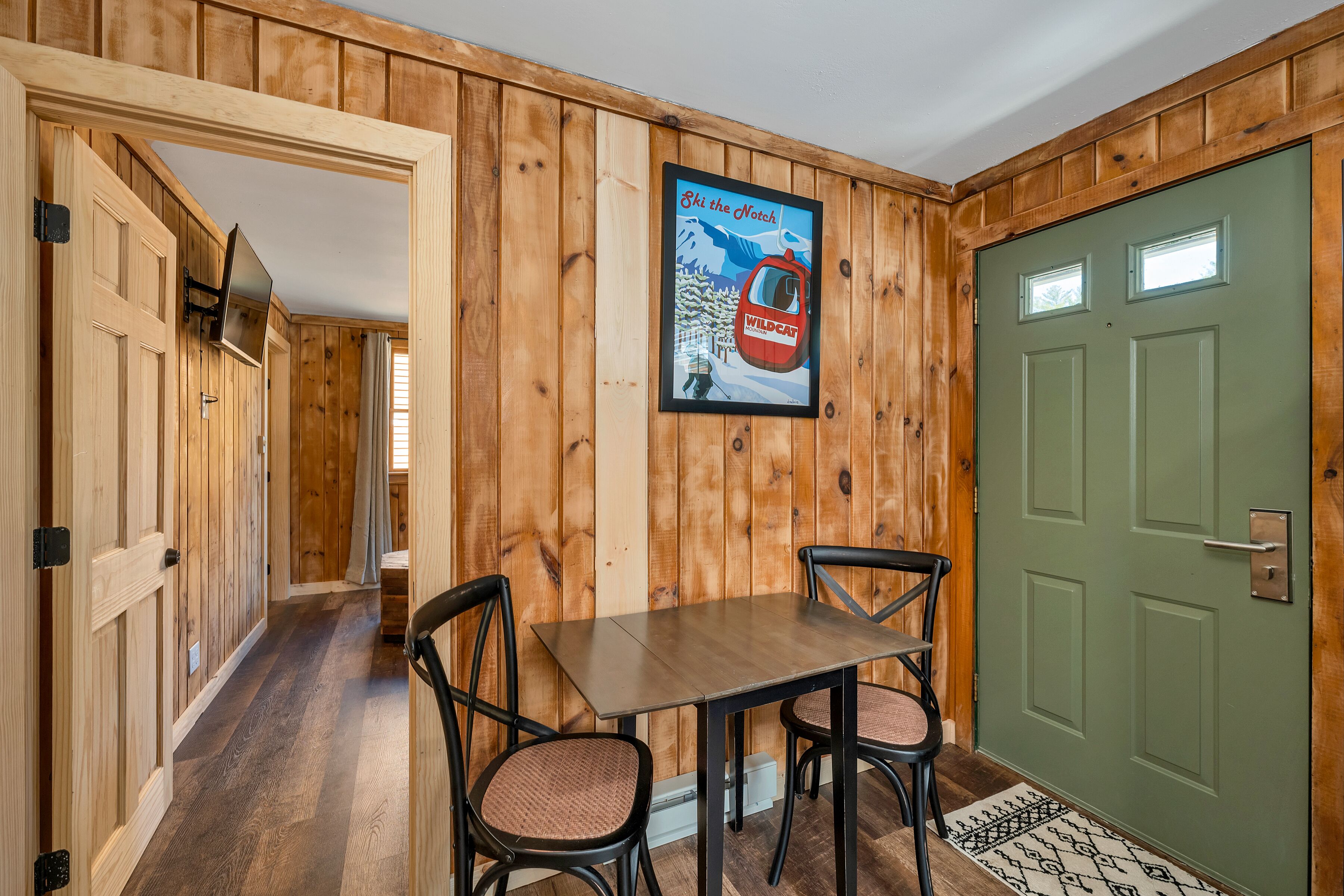 Ein Holzinterieur mit einem Esstisch, Stühlen, einer grünen Tür und einem Skiaffiche.