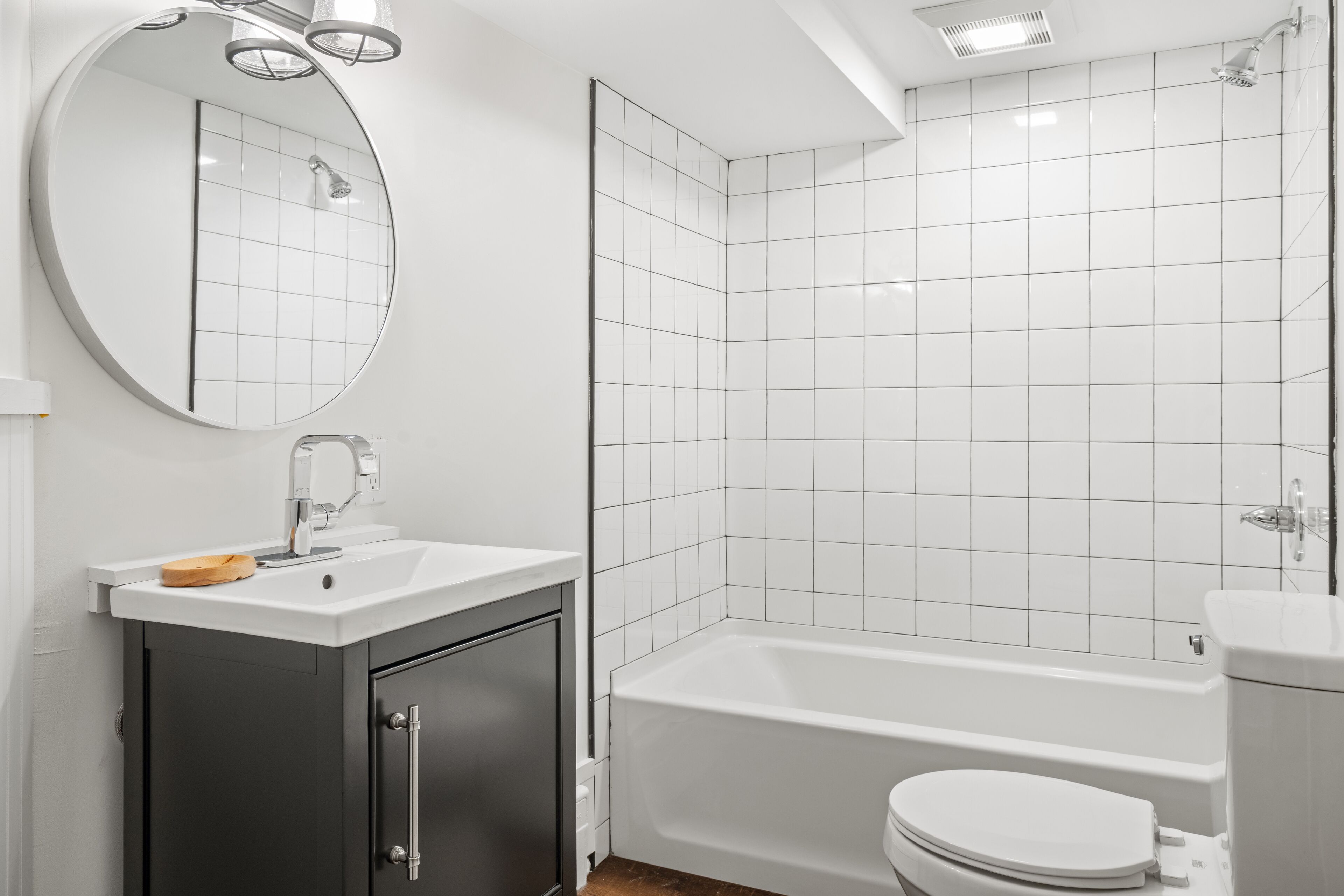 A modern bathroom with a white sink, mirror, and bathtub.