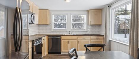 A modern kitchen with wooden cabinets, a stainless steel refrigerator, a dishwasher, and a dining table with chairs.