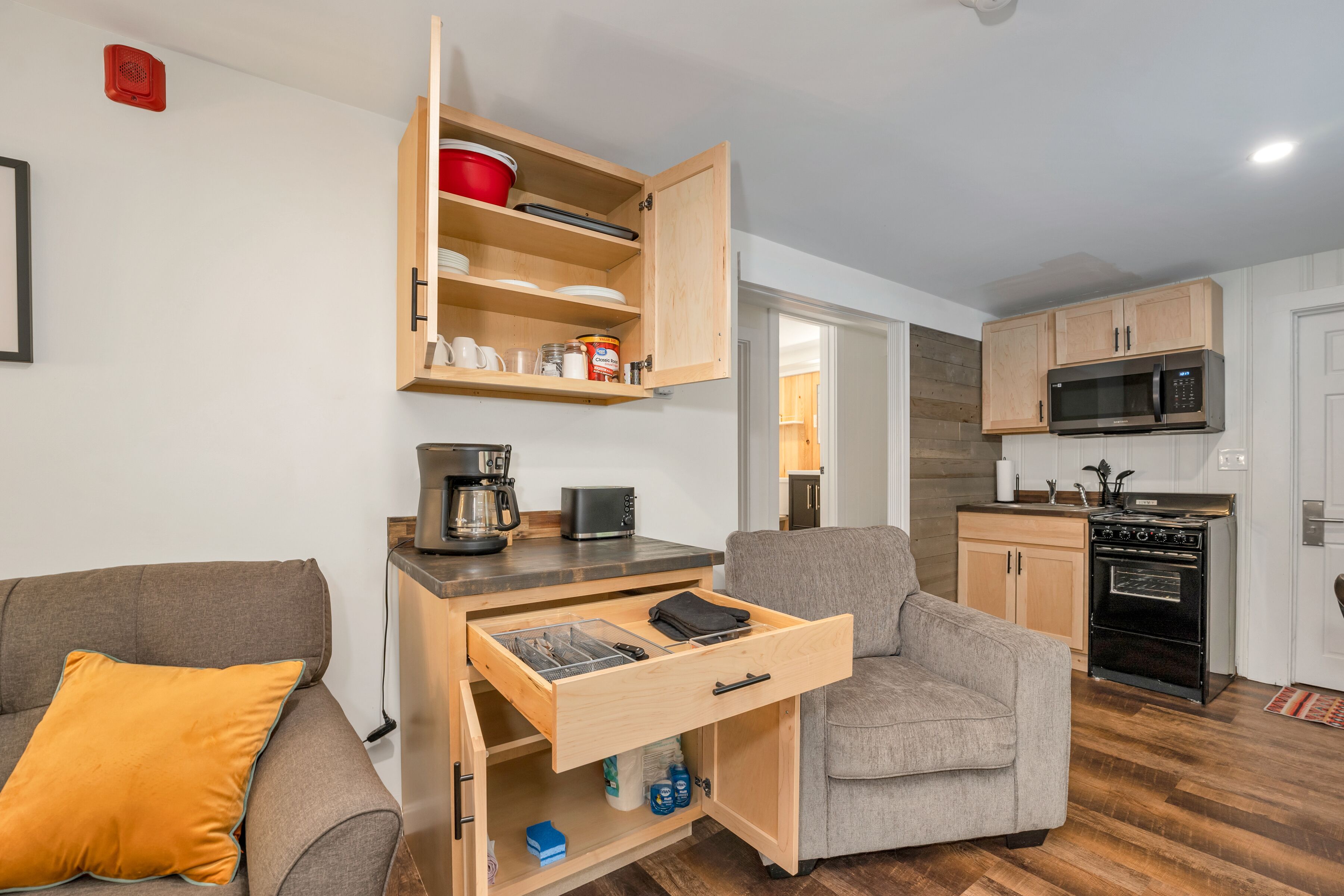 A compact living space with a kitchenette, a sofa, and a wooden cabinet with drawers.
