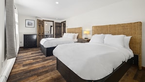 Habitación de hotel con dos camas, suelo de madera, un aparador, un escritorio y una lámpara.