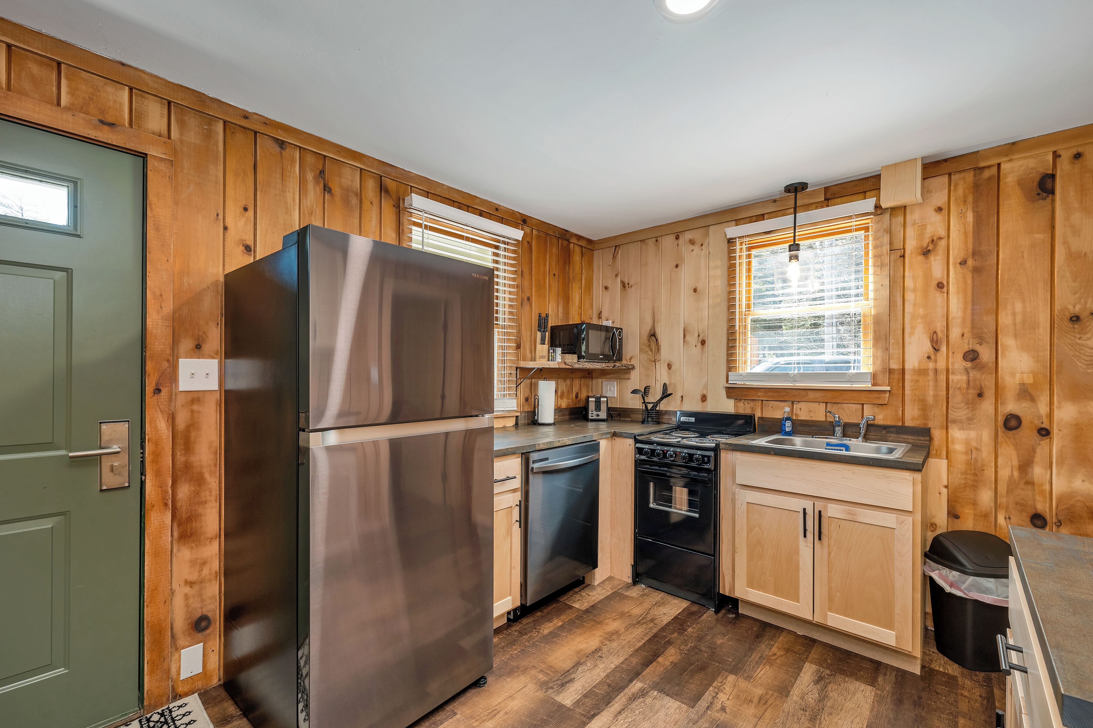 A compact kitchen with wooden paneling, a stainless steel refrigerator, a dishwasher, an oven, and a sink.