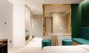 A modern hotel room with a large bed, a vanity with a mirror, and teal accent chairs.