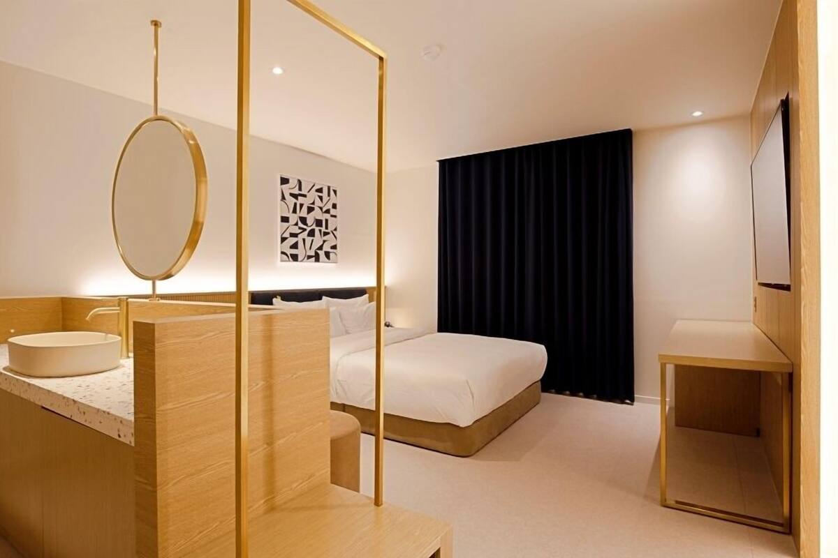 A modern hotel room with a wooden vanity, a large bed, a black curtain, and a wall-mounted artwork.