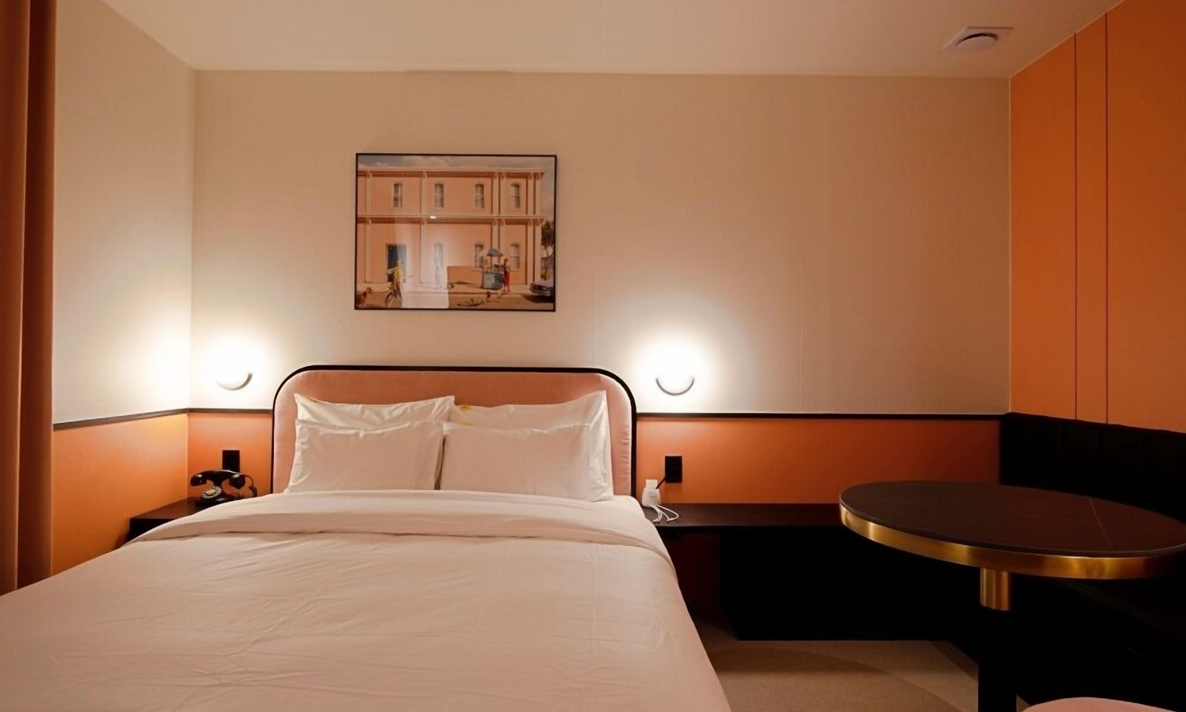 A hotel room with a bed, bedside tables, a round table, and a wall-mounted painting.