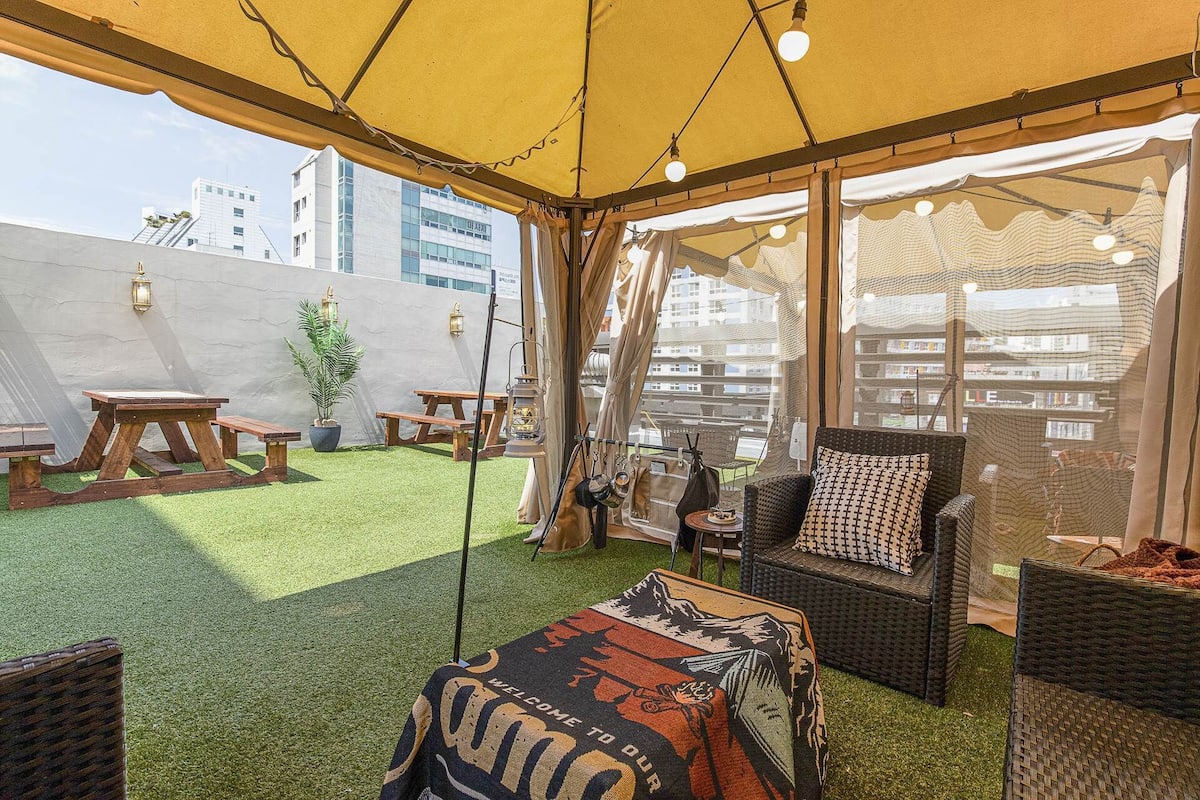 An outdoor patio with a yellow canopy, wicker furniture, and a view of the cityscape.