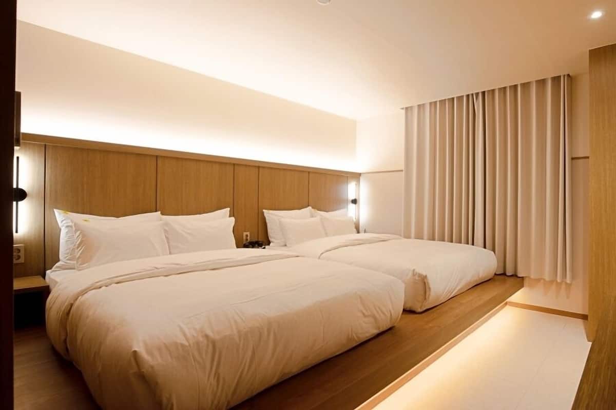 A modern hotel room with a large bed, wooden headboard, and a large window with curtains.