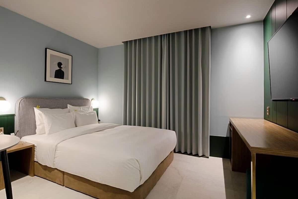 A modern hotel room with a large bed, bedside tables, a desk, and a television.