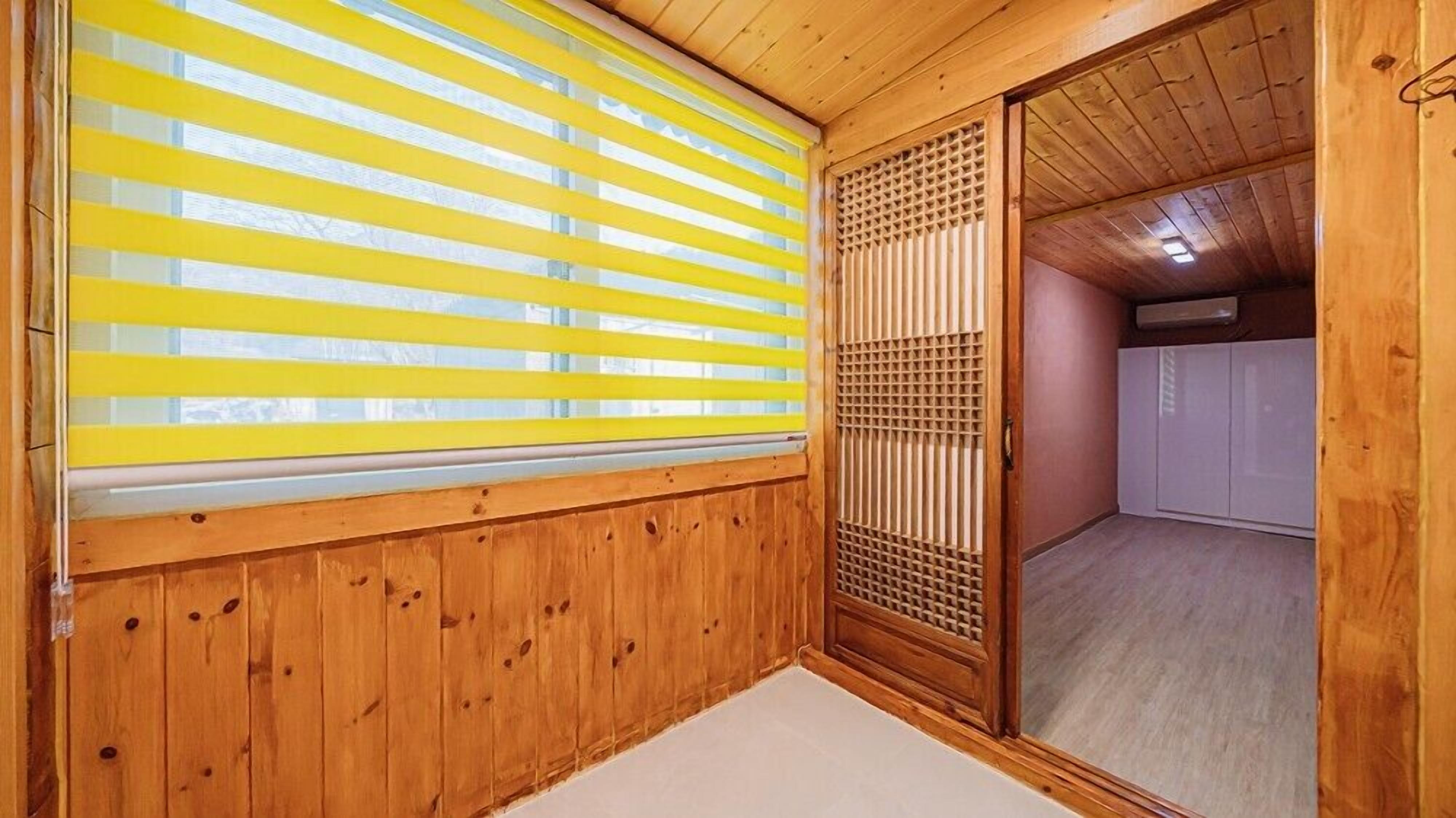 A traditional Japanese room with wooden walls, a sliding door, and a window with yellow blinds.