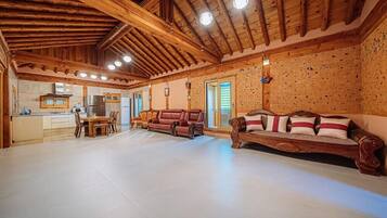 A spacious living area with a wooden ceiling, a dining table with chairs, a sofa, and a kitchen area with a refrigerator and stove.