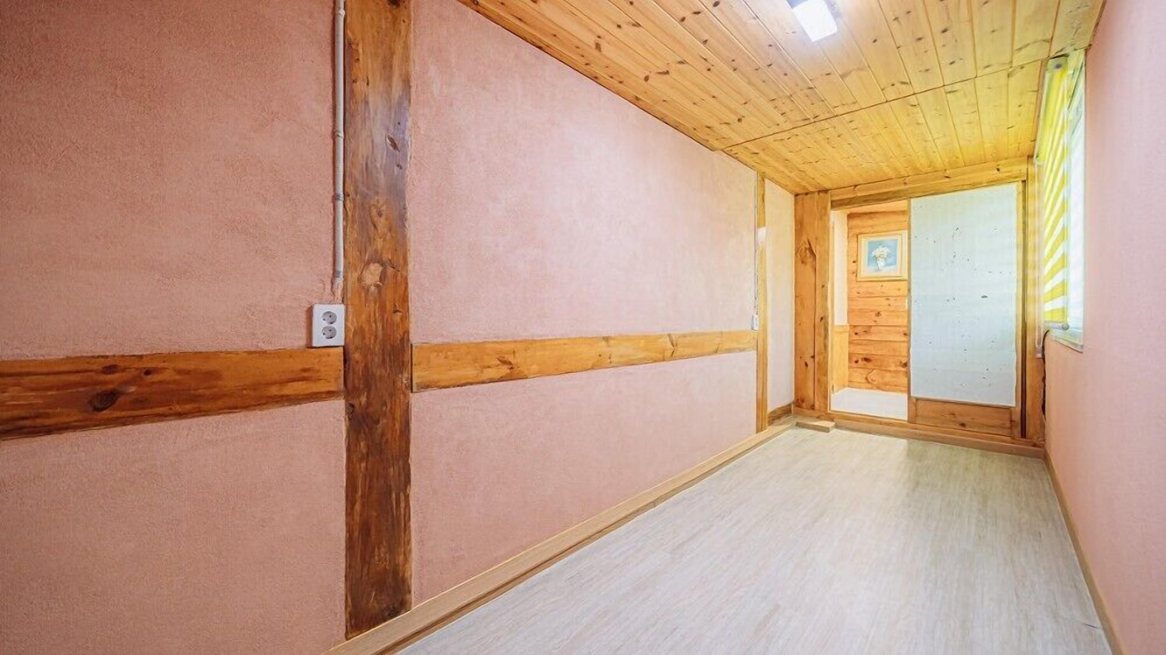 A hallway with wooden beams, a light-colored floor, and a door at the end.