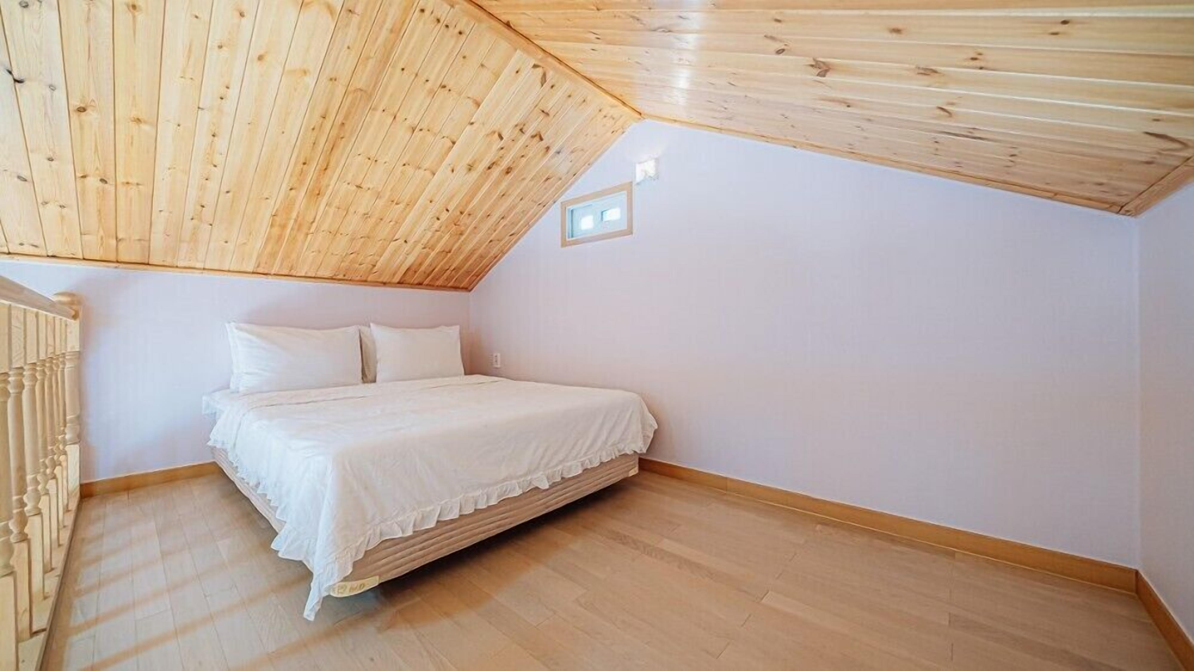 A bedroom with a sloped ceiling, a bed, and a window.