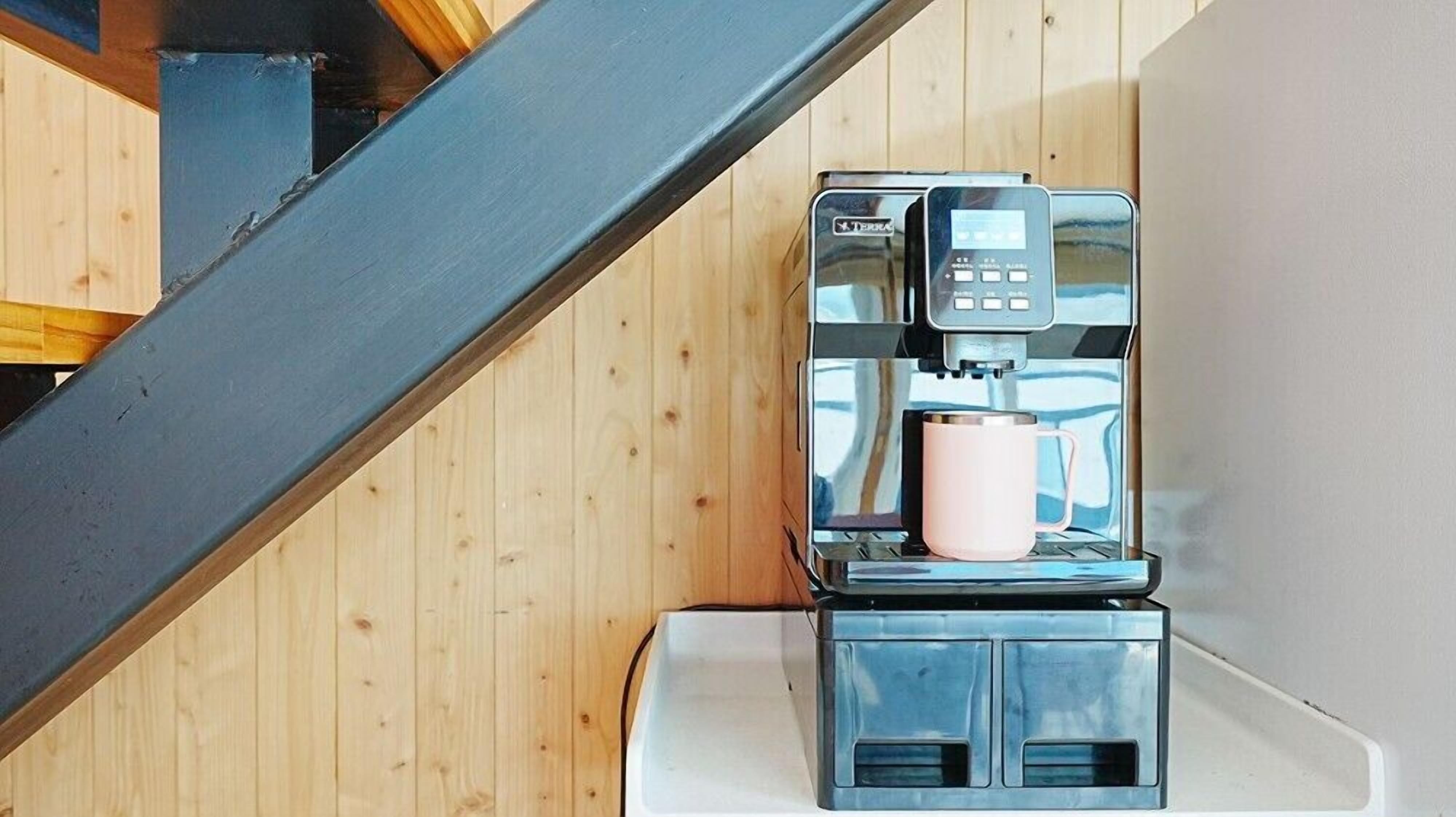 A coffee machine with a digital interface and a pink mug on a white surface.